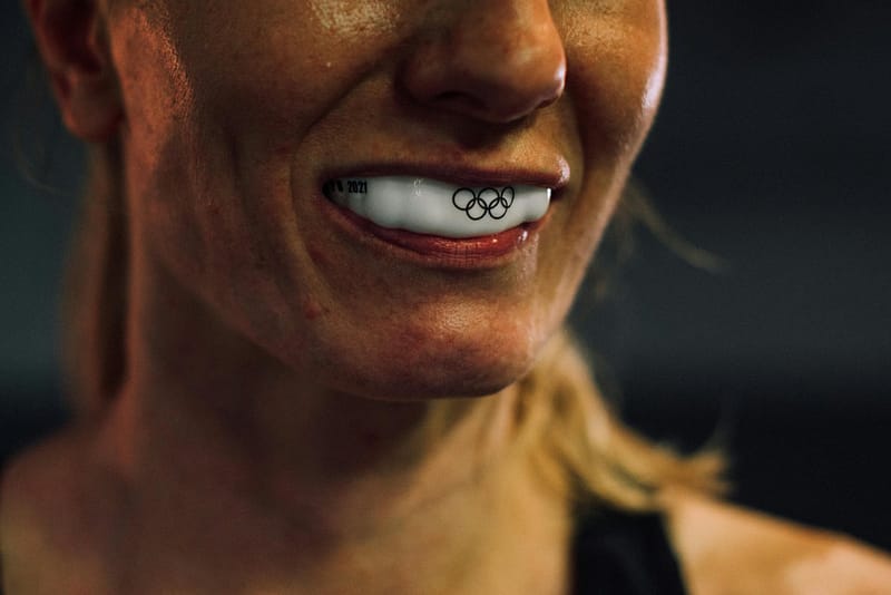 Close-up of a female boxer smiling with a white mouthguard featuring the Olympic rings and 2021 text