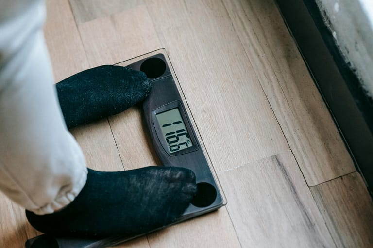 Person wearing black socks stands on a digital scale displaying 116.6 kilograms on a wood floor.