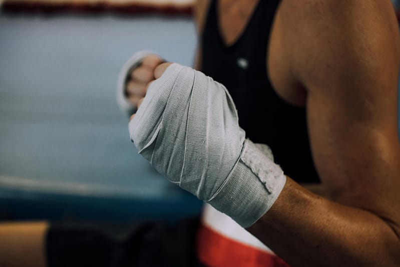 Close-up of a boxer's fists wrapped in white hand wraps inside a boxing gym.