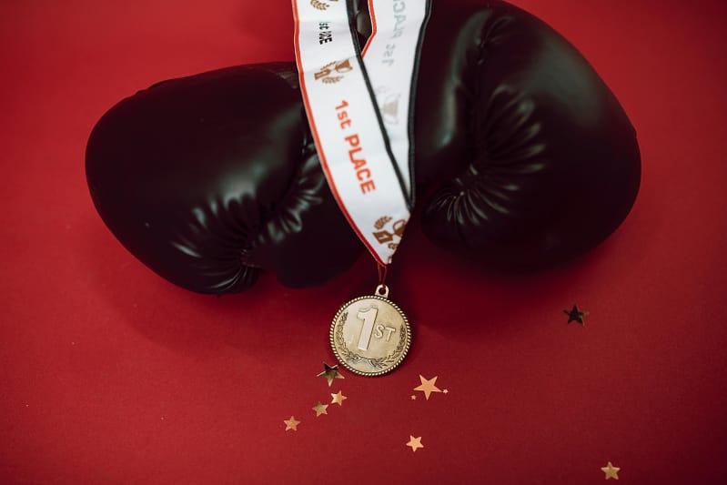 Black boxing gloves with a gold first-place medal on a red background.