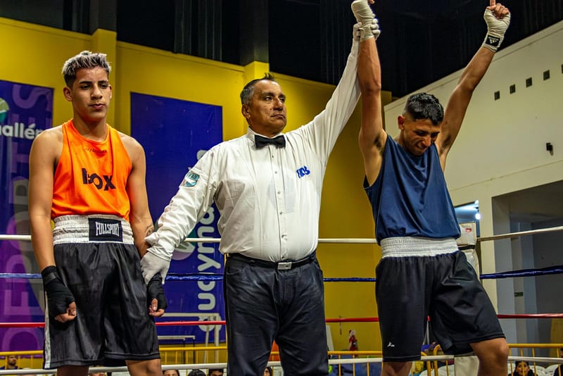Referee raises the winning boxer’s hand in the ring after a technical decision, other fighter standing beside.
