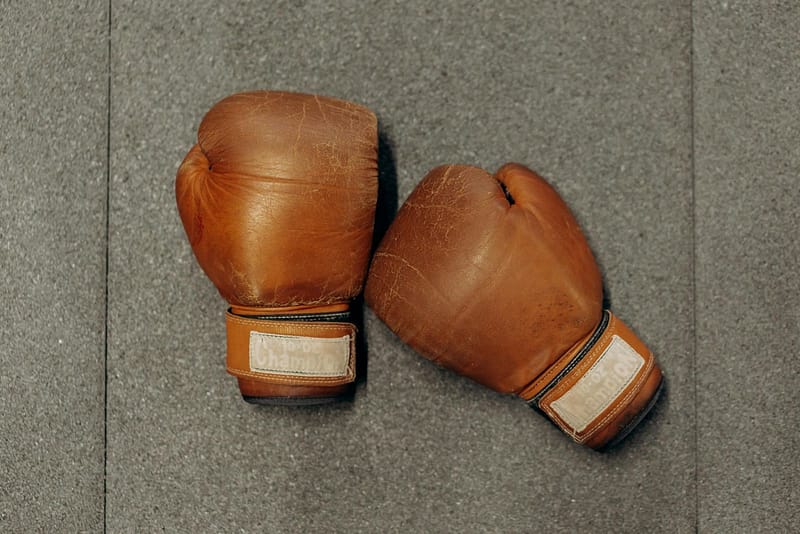 Worn brown leather boxing gloves resting on a gym floor, illustrating why referees wipe gloves clean of canvas grit during a fight.