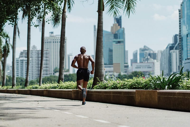 A boxer running roadwork on a city pathway during weight cut training, illustrating the physical effort required to make weight before a fight.