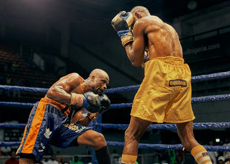 Two boxers exchange punches in the ring during a match, with one fighter crouching low and the other covering up.